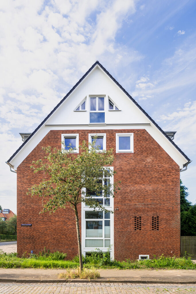 Straßenseitige Giebelfront des aufgestockten Wohn- und Geschäftshauses mit neuen Gauben, weißem Dachbereich und moderner Fensterstruktur.