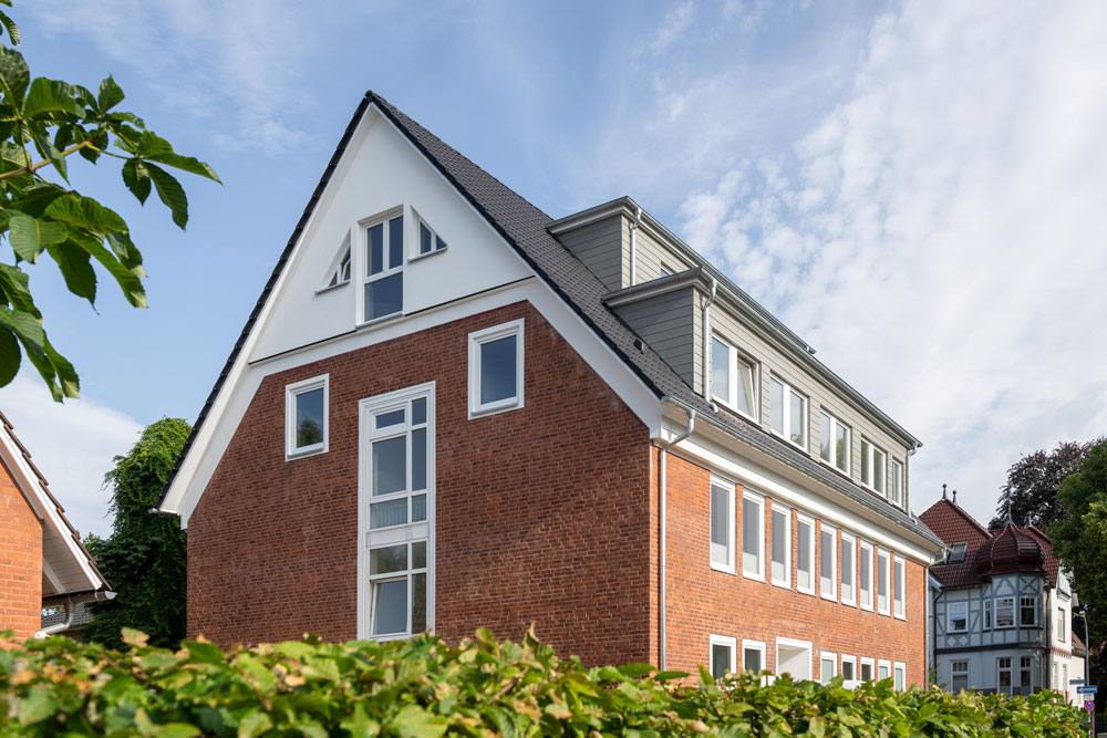 Frontal seitliche Ansicht eines modernen drei stöckigen Hauses, hinter einer Grünhecke bei schönem Wetter